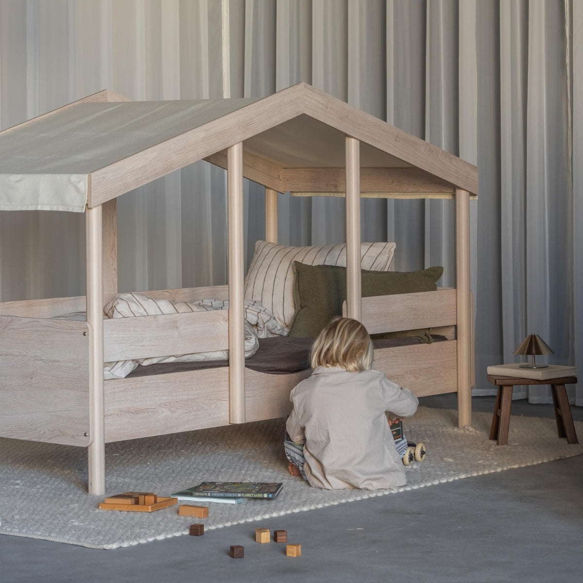 Quax Cottage Montessori House Bed 90 x 200cm with Butter fabric roof and child playing beside the bed