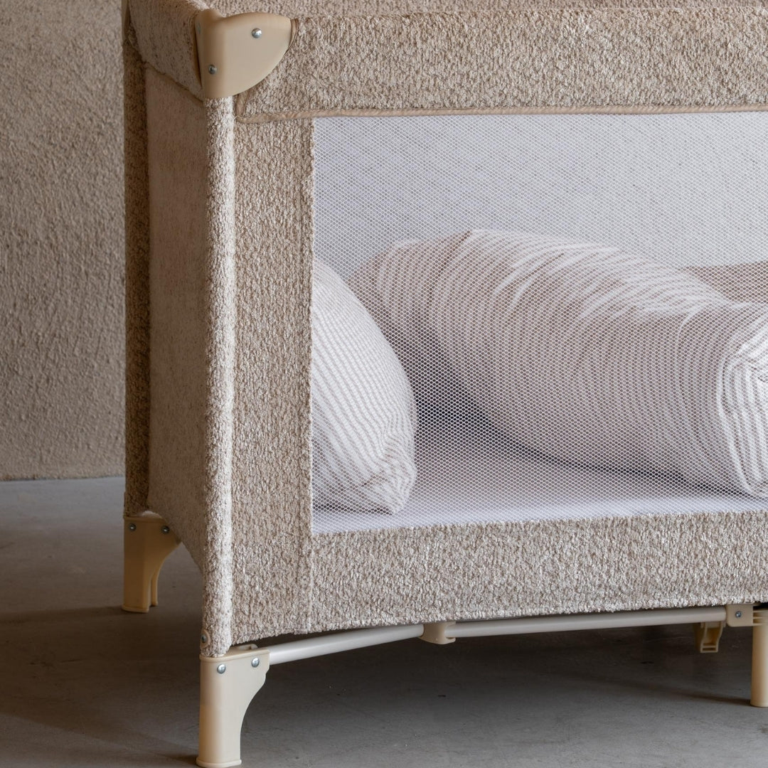 Quax travel cot with soft sheep boucle fabric with breathable white mesh sides and comfy mattress and pillows close up view in modern scandi room