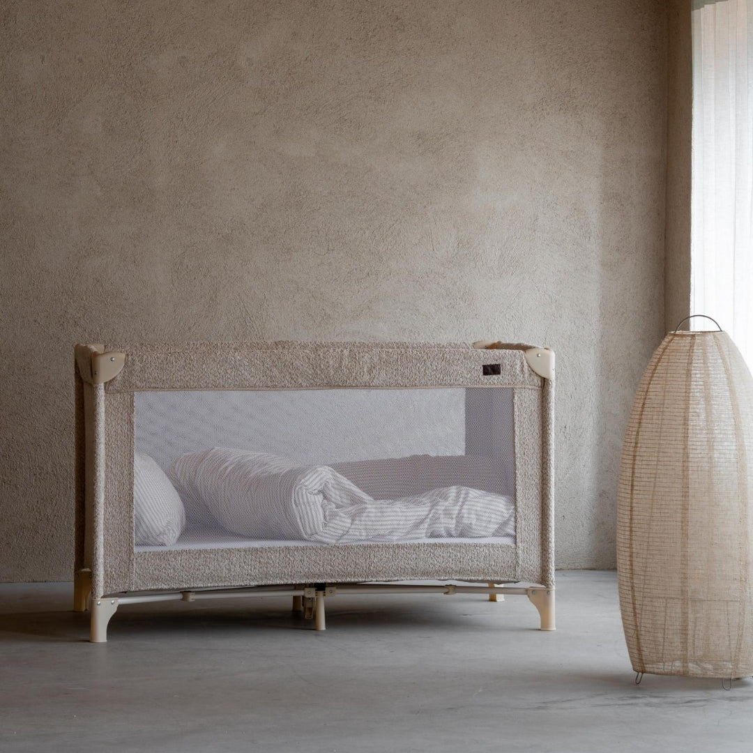 Quax travel cot with soft sheep boucle fabric in a minimalistic scandi european room with a neutral wall and floor.