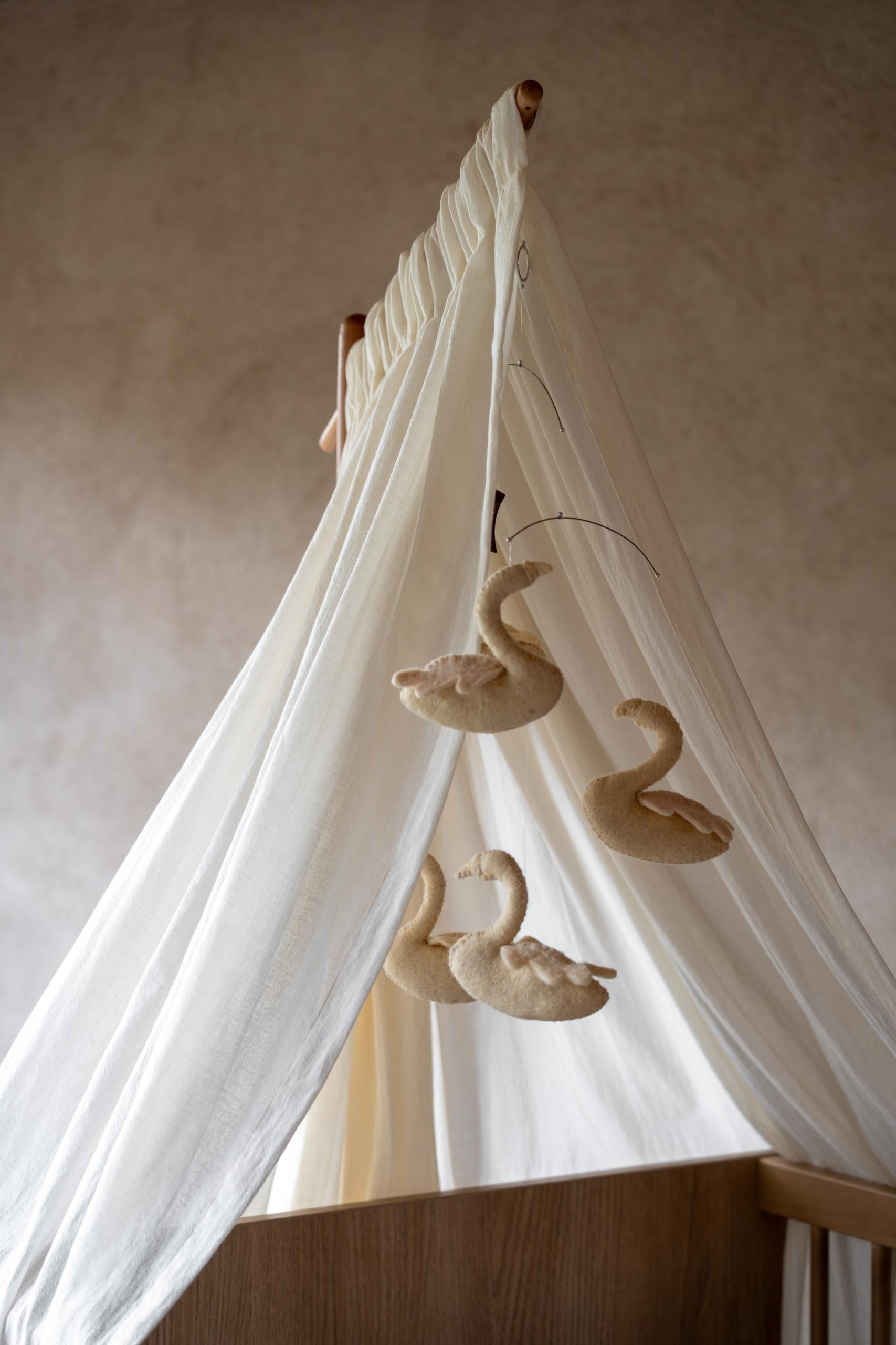quax butter canopy veil with swan decorations hanging from a wooden frame over baby cot bed against a neutral wall.