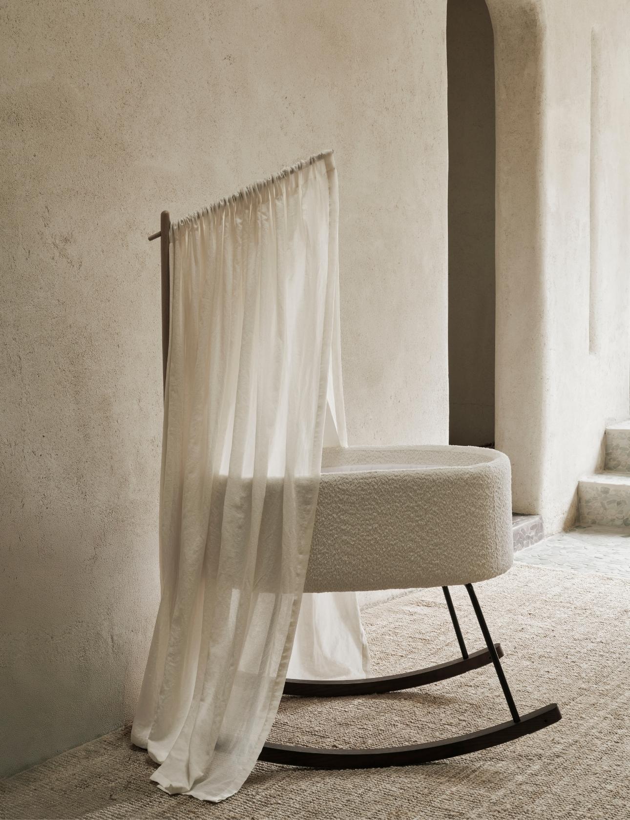 quax butter canopy veil hanging from a wooden frame over a boucle fabric rocking cradle deluxe for baby against a neutral wall.