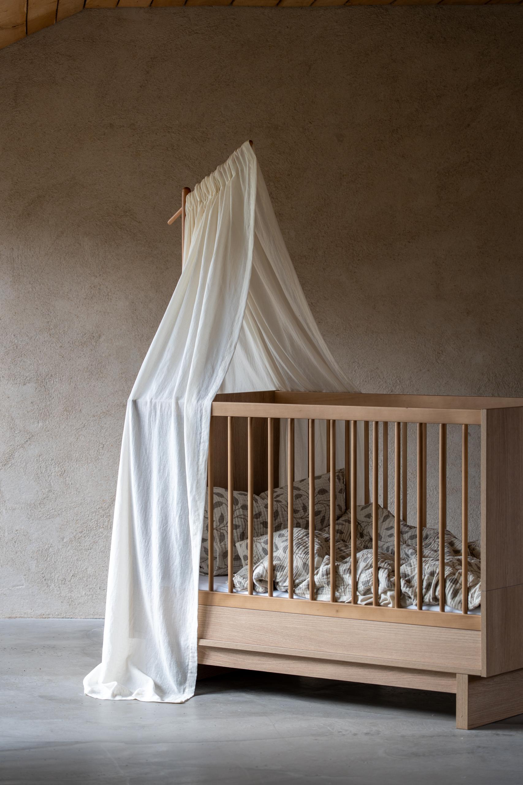 quax butter canopy veil hanging from a wooden frame over a scandi wooden cot bed against a neutral wall.