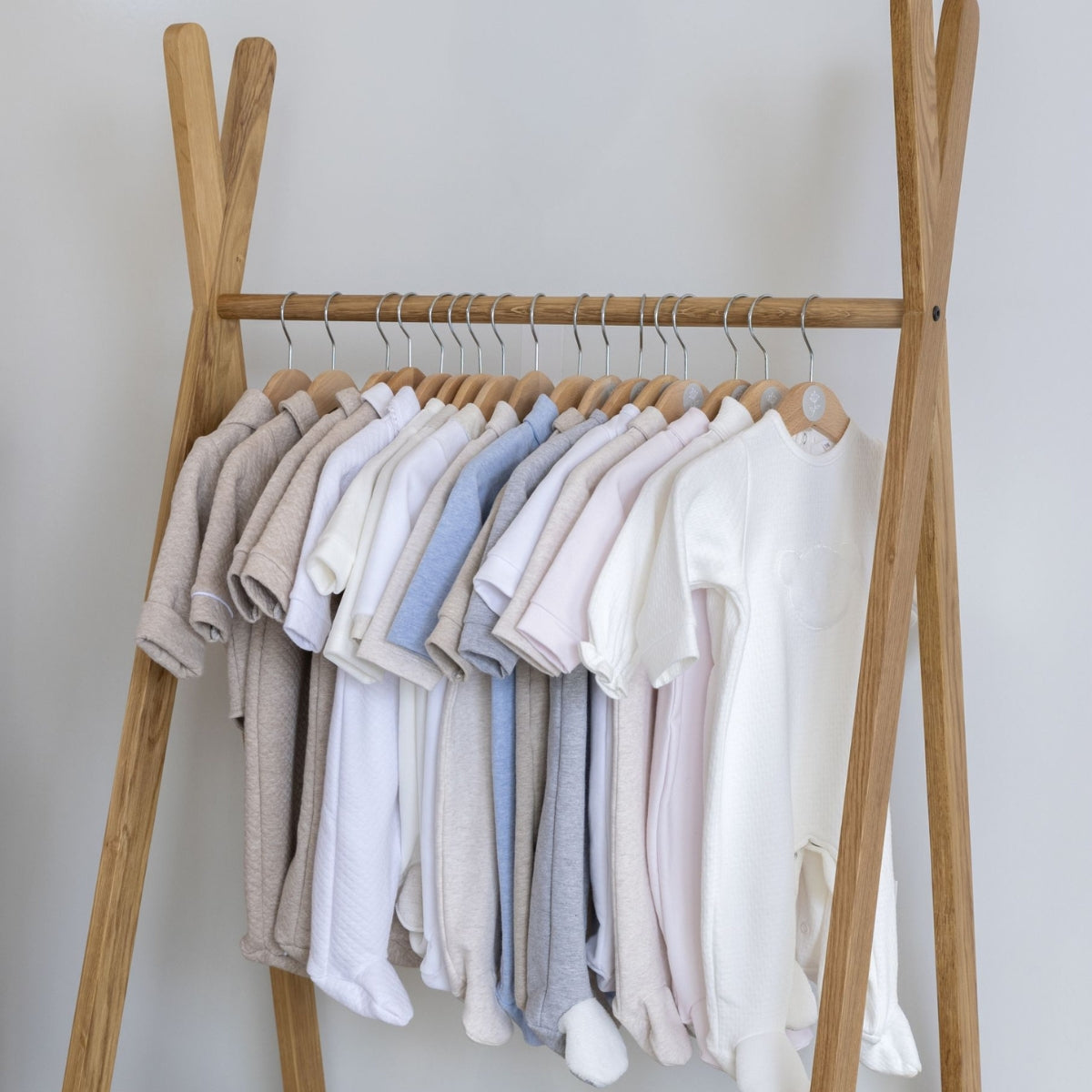 solid oak Wood clothing rail with a variety of baby clothes on hangers against a plain background